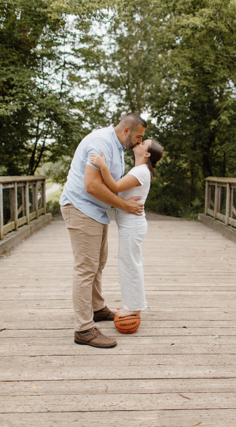Couple sharing a kiss on a footbridge, basketball at their feet — Home Team Photography