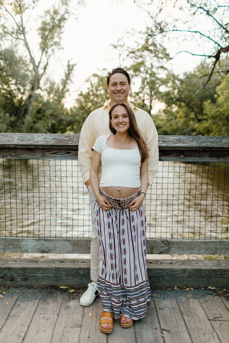 Expectant couple on a wooden footbridge over the river — maternity portrait by Home Team Photography