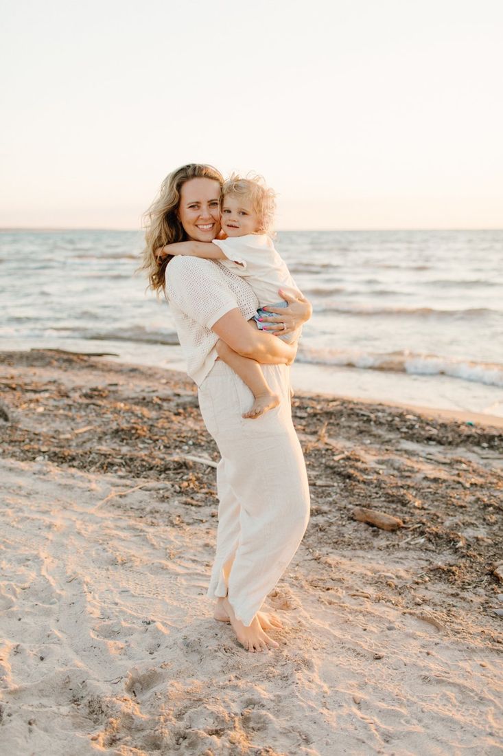 Mother holding her toddler on the beach at golden hour — Home Team Photography