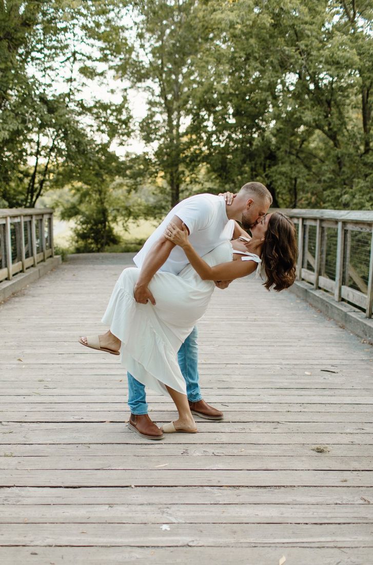 Couple sharing a dip kiss on a wooden footbridge at golden hour — Home Team Photography
