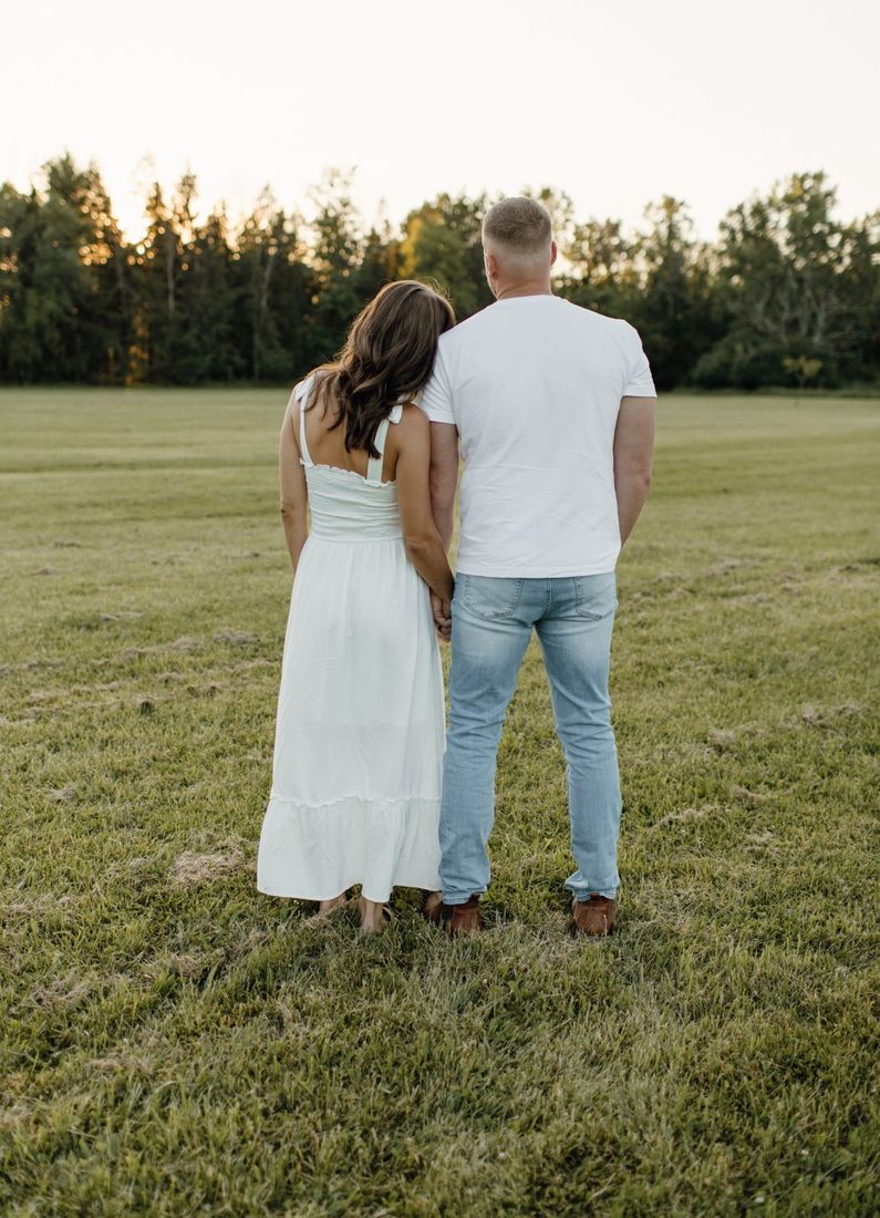 Couple holding hands in a golden-hour field — engagement portrait by Home Team Photography