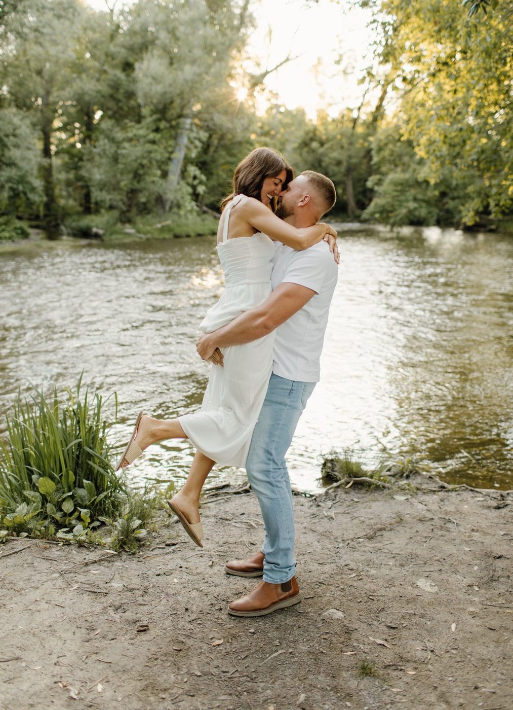 Man lifting his partner by the river at golden hour — engagement portrait by Home Team Photography