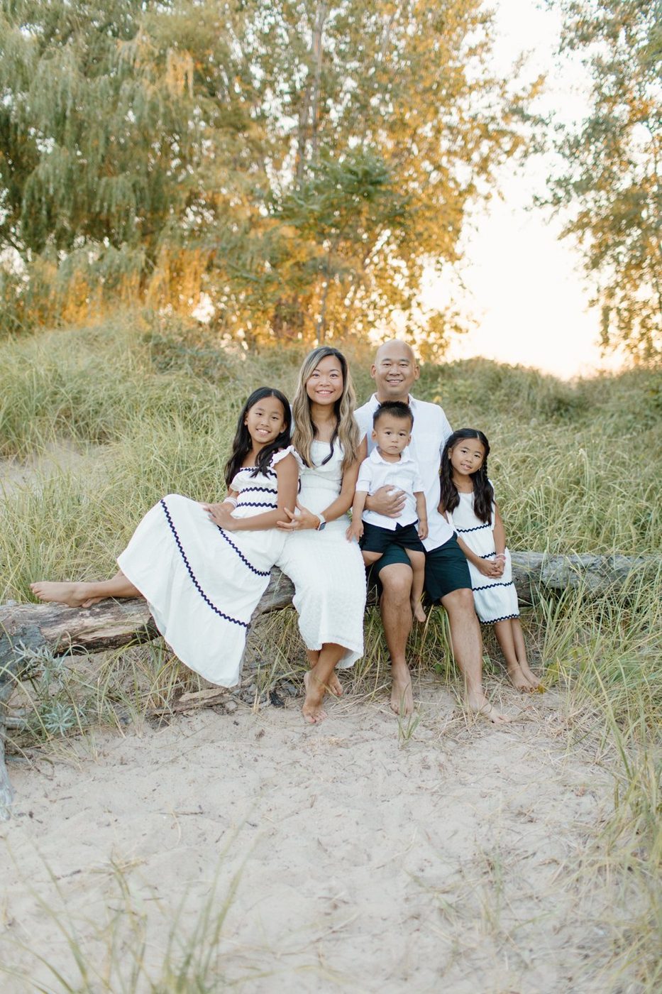 Family of five sitting on a driftwood log in the dune grass at golden hour — Home Team Photography